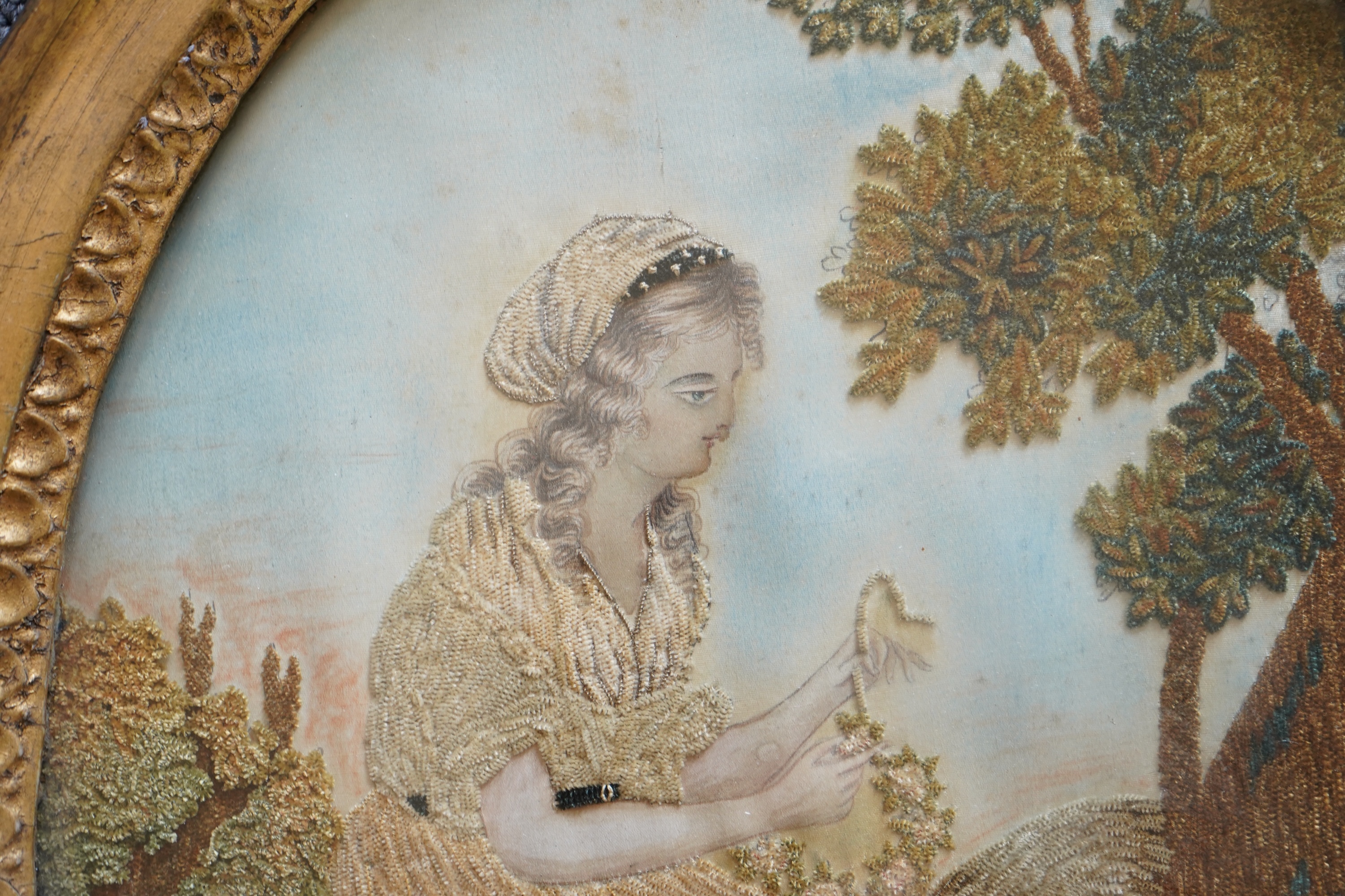A pair of unusual early 19th century oval silk Chenille embroideries, one depicting a seated lady surrounded by a lion and donkey, the other depicting a seated shepherdess under tree with two sheep. Both have water colou